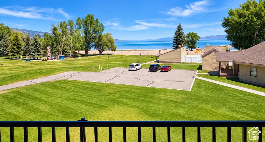 Lush green lawn with paved pathways and a dedicated parking area, featuring mature trees and a distant body of water