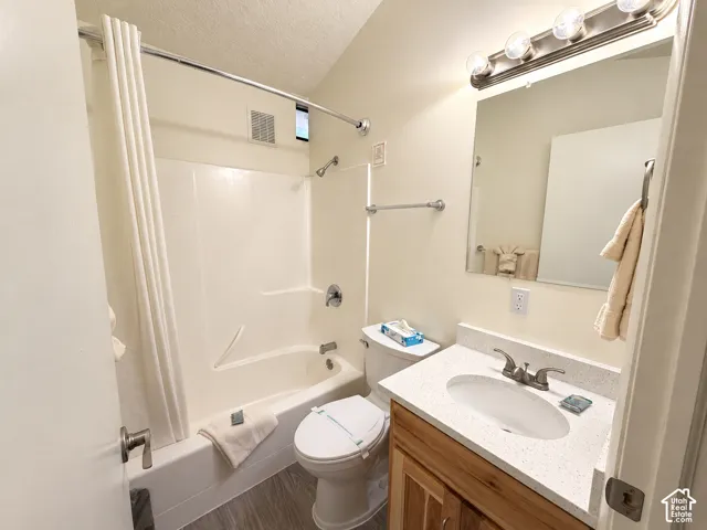 Bathroom featuring a shower-tub combination, vanity with a white countertop, wood-finish cabinetry, and a wall-mounted mirror with overhead lighting