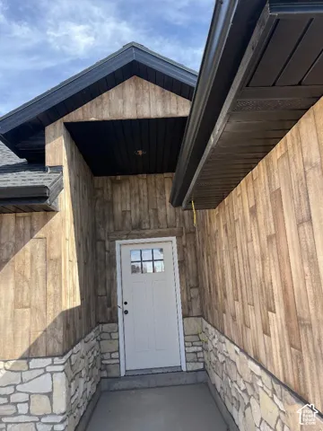 Entryway featuring a white door with upper window panes, stone veneer base, wood-finish siding, and dark soffit