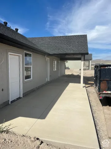 Exterior featuring stucco siding, white-framed windows, a covered concrete walkway, and an asphalt shingle roof