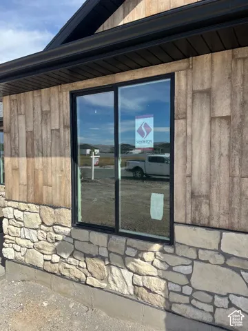 Exterior featuring stacked stone base, vertical wood-finish siding, black frame windows, and dark gutters