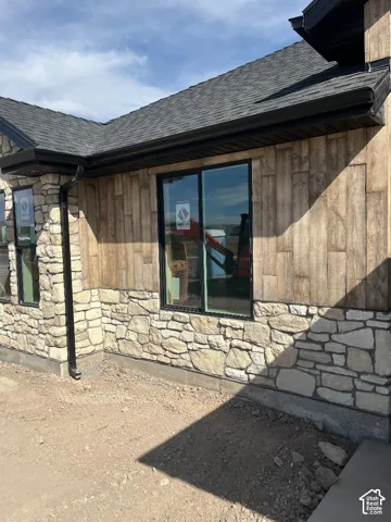 Stone veneer and wood-finish siding exterior with black-framed windows, black gutters, and a dark shingle roof