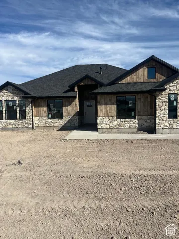 Stone and wood-finish siding exterior with black-framed windows, a dark shingle roof, and a concrete walkway