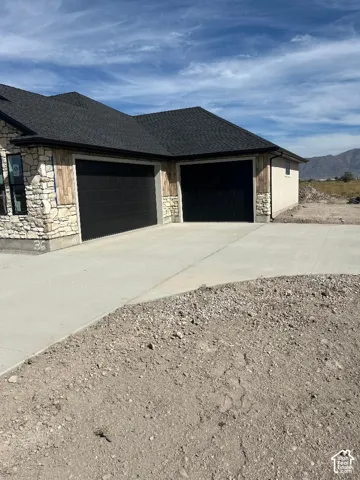 Exterior featuring stone and wood-finish siding, a dark shingle roof, and dual black garage doors