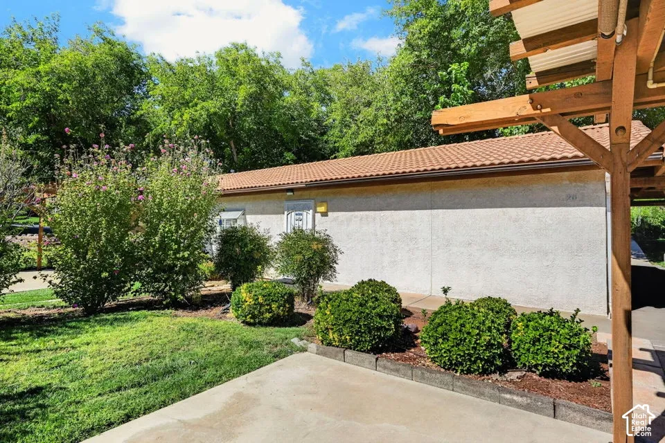 Stucco exterior with a tiled roof, surrounded by mature landscaping and a wooden pergola structure