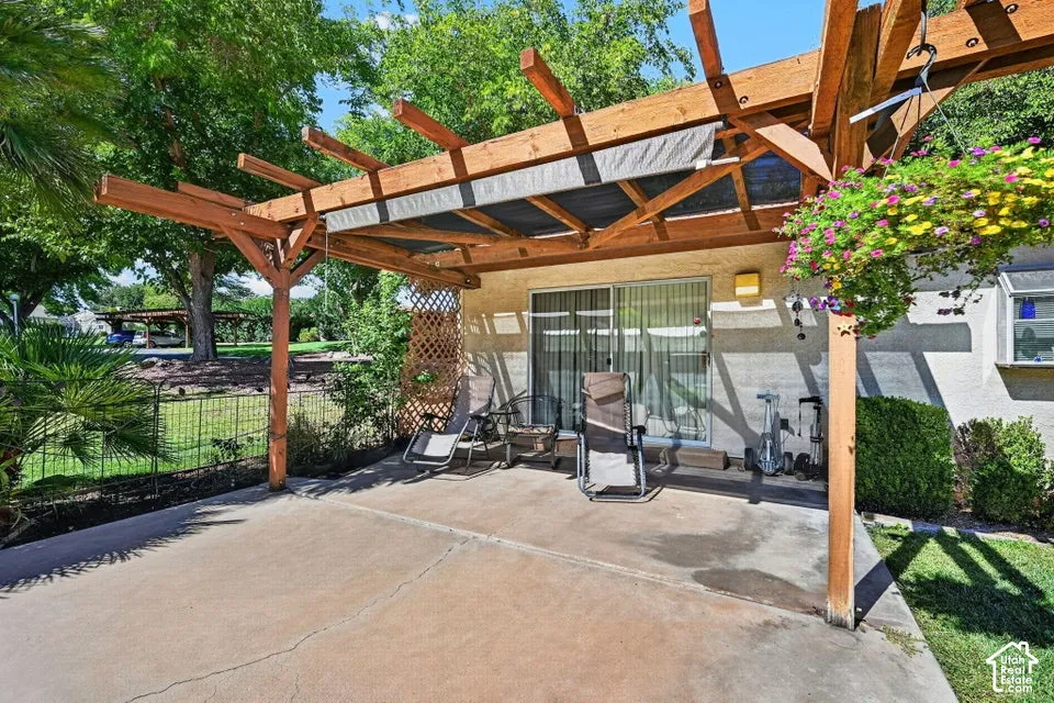 Expansive concrete patio with a wooden pergola, retractable shade cover, and direct access through a sliding glass door