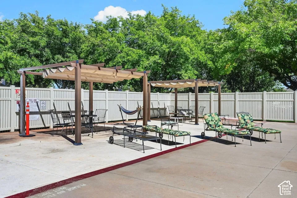 Outdoor patio area with two pergolas, concrete surfacing, and a white privacy fence
