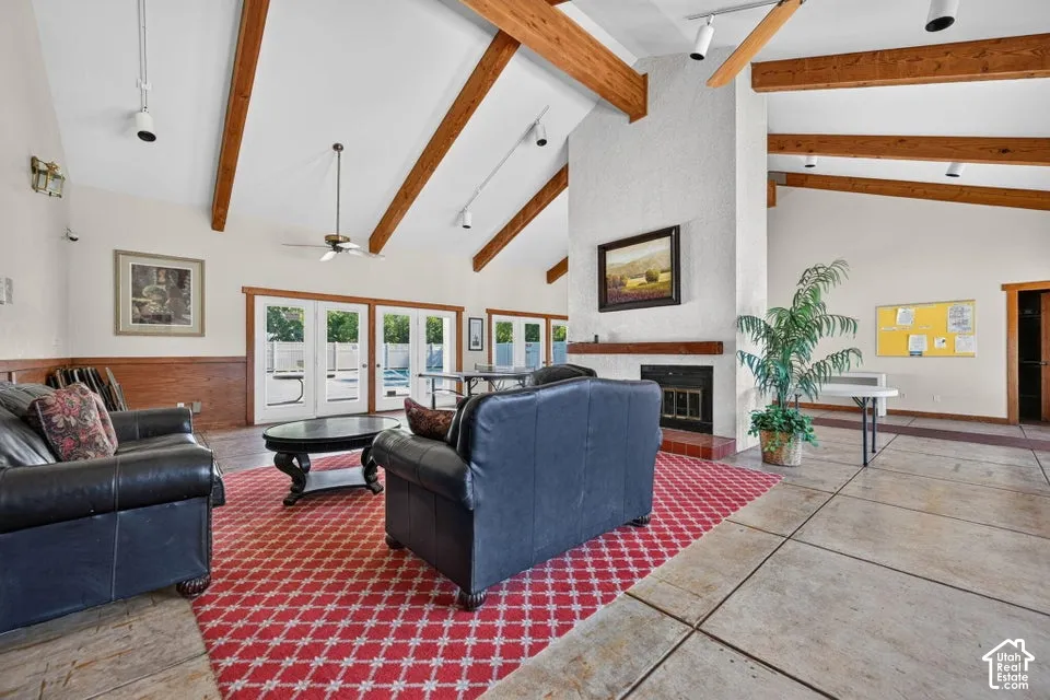 Vaulted ceiling with exposed wood beams, white textured fireplace, built-in wood mantel, and multiple sets of French doors