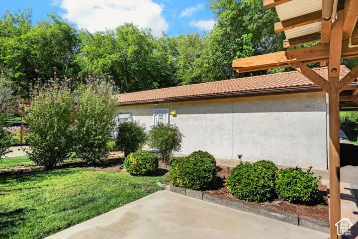 Stucco exterior with a tiled roof, surrounded by mature landscaping and a wooden pergola structure