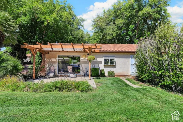 Expansive backyard featuring a manicured lawn, established landscaping, a concrete patio, a wood pergola, and a tile roof