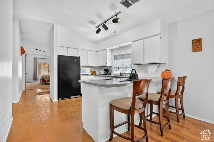 Kitchen featuring white cabinetry, track lighting, a peninsula with counter seating, and tile flooring