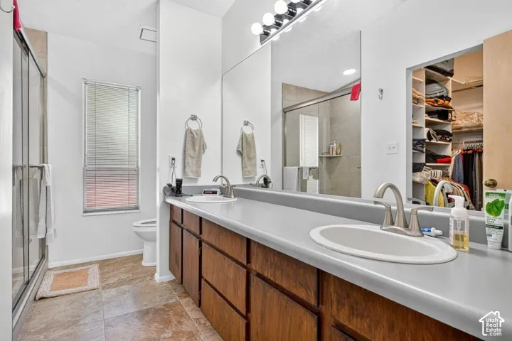 Dual vanity with undermount sinks, wood-finish cabinetry, a large mirror, and an adjacent walk-in shower with a sliding glass door