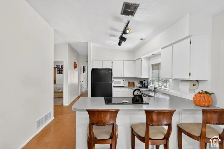 Kitchen featuring white cabinetry, track lighting, a built-in electric cooktop, and an integrated kitchen island with a light-toned countertop