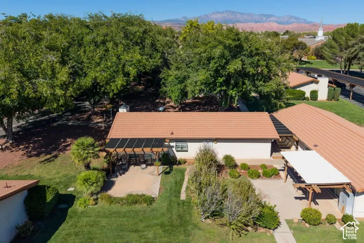 Terracotta tile roof, attached covered patio with pergola, open concrete patio, expansive green lawn, and mature trees