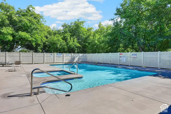 Swimming pool with integrated spa and stainless steel handrails, surrounded by concrete decking and a slatted privacy fence