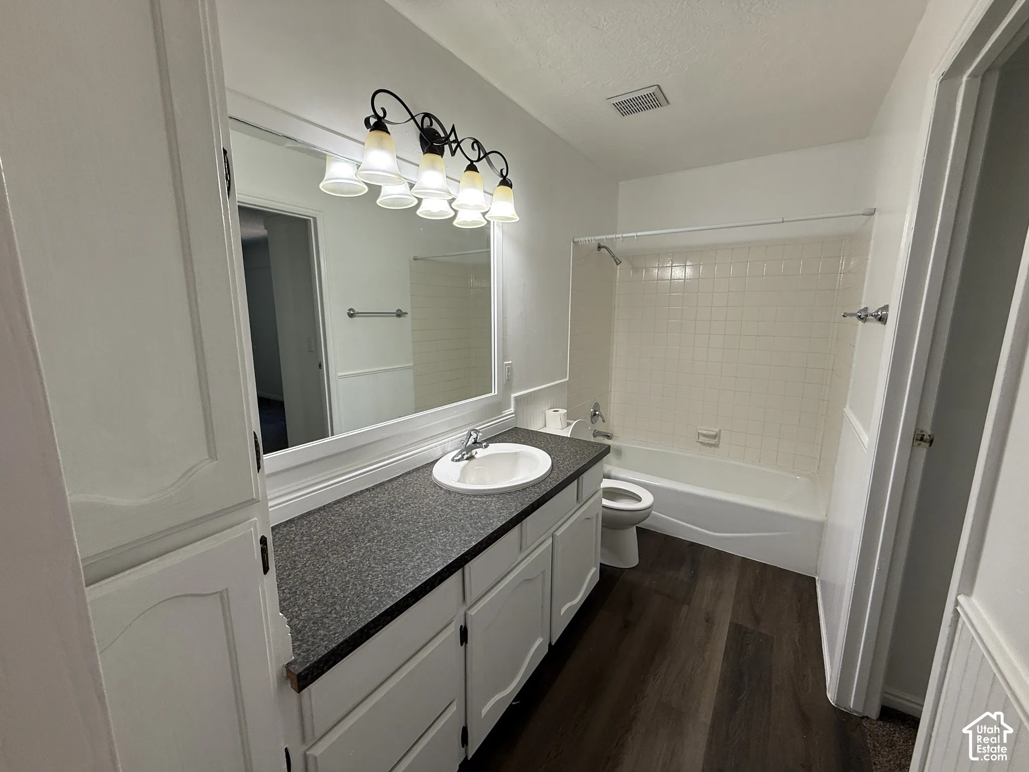 Bathroom featuring wood-finish flooring, a white vanity with an integrated sink, a dark speckled countertop, and a built-in tub with a tiled surround