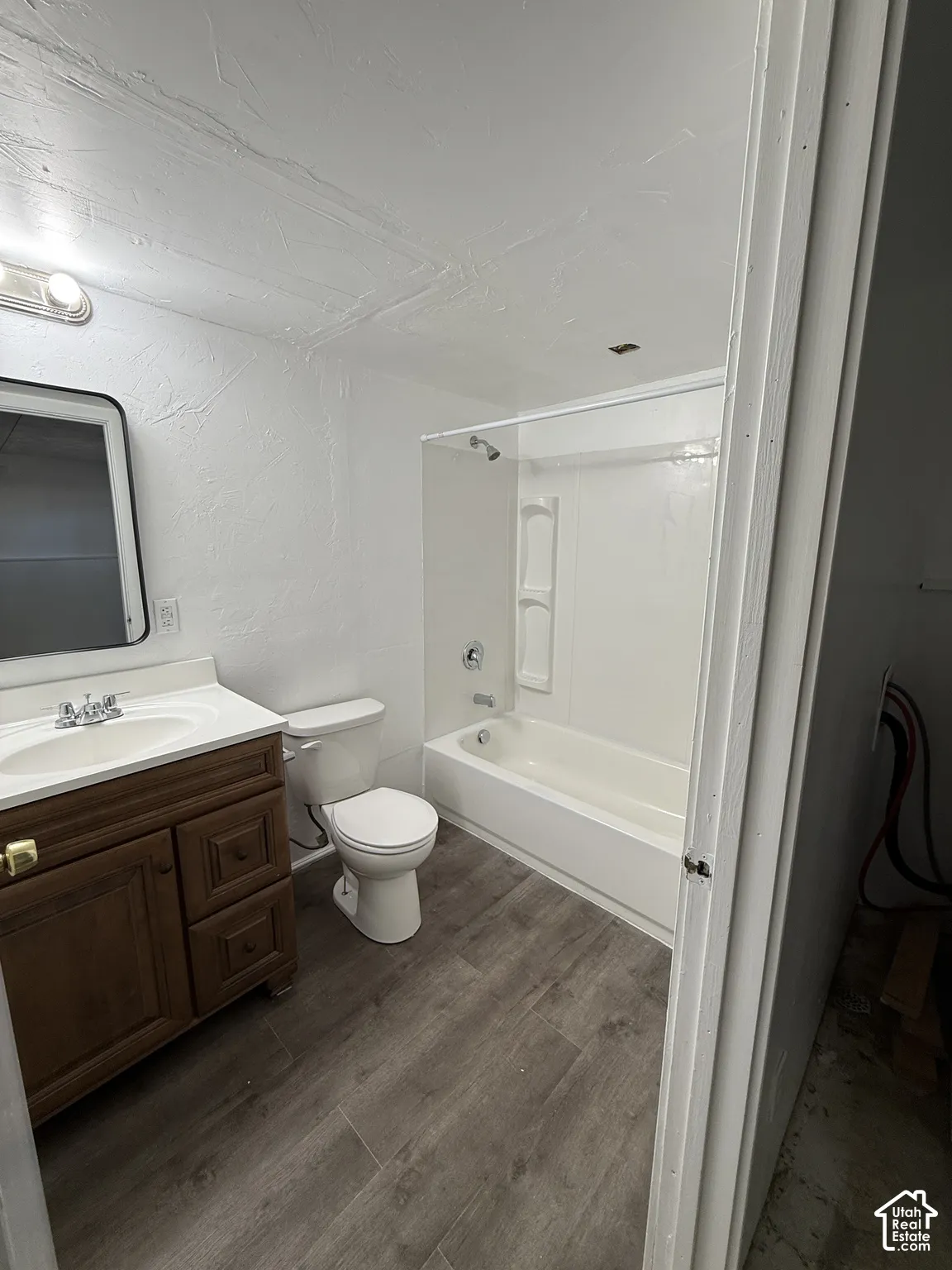 Wood-finish flooring, white vanity with integrated sink, white toilet, and a white tub with integrated shower