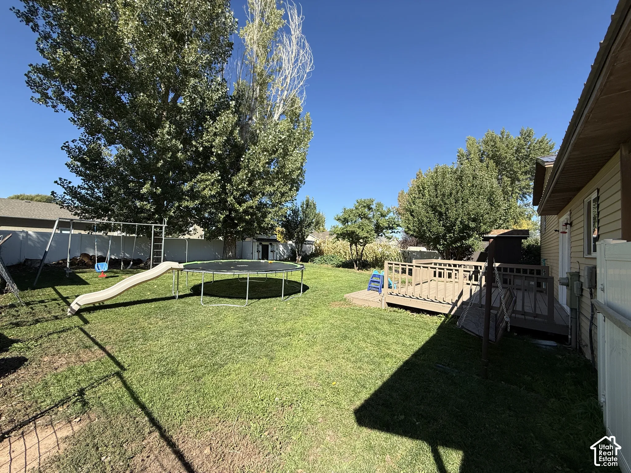 Expansive backyard featuring a green lawn, mature trees, and a wooden deck