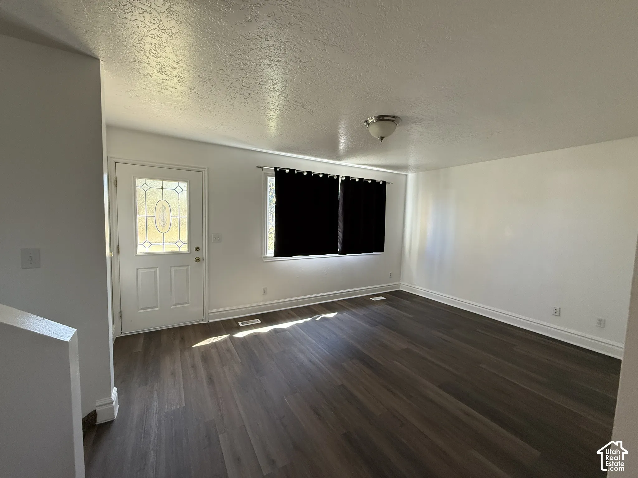 Hardwood-look flooring, white walls, decorative glass entry door, window with white trim, and a ceiling-mounted light fixture