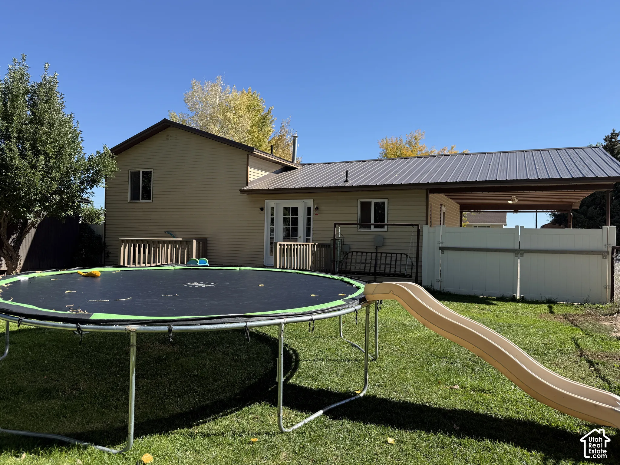 Rear exterior featuring tan siding, a gray metal roof, covered patio, and a grass lawn