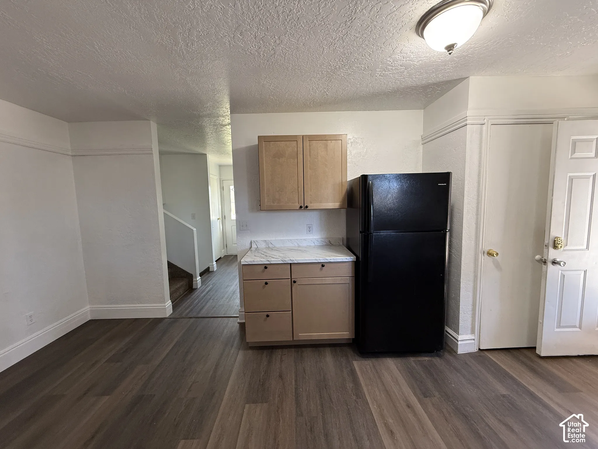 Wood-finish flooring, light-colored cabinetry, white countertops, and a black refrigerator