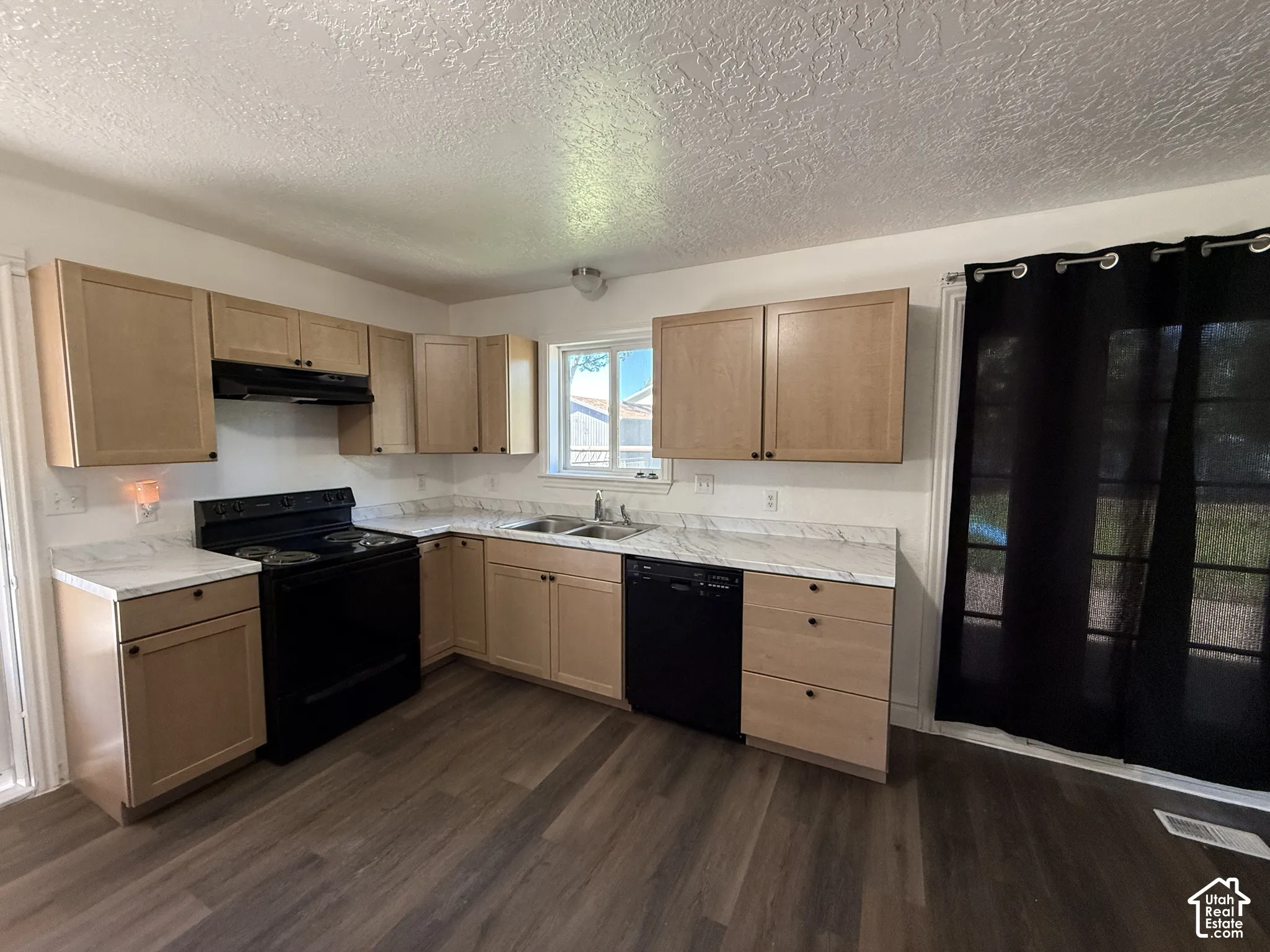 Kitchen featuring light wood-finish cabinetry, white countertops with veining, black appliances, and wood-finish flooring