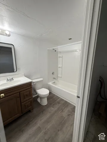 Wood-finish flooring, white vanity with integrated sink, white toilet, and a white tub with integrated shower