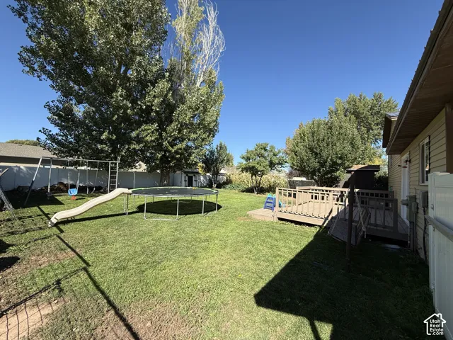 Expansive backyard featuring a green lawn, mature trees, and a wooden deck