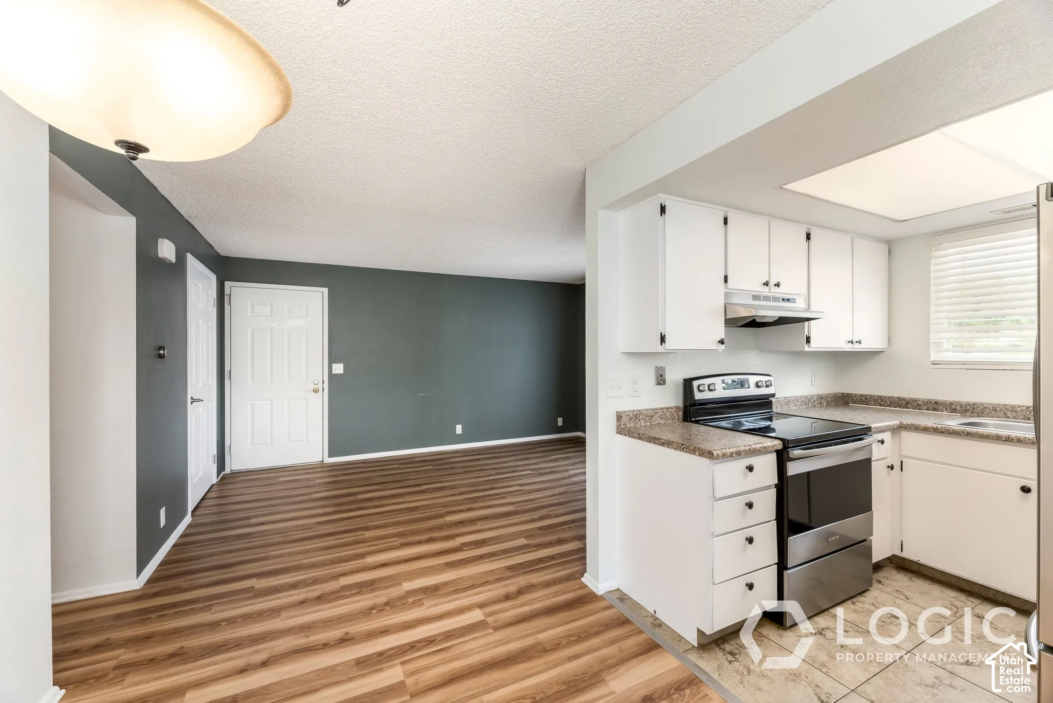 Kitchen featuring white cabinetry, stone-look countertops, stainless steel appliances, and wood-finish flooring