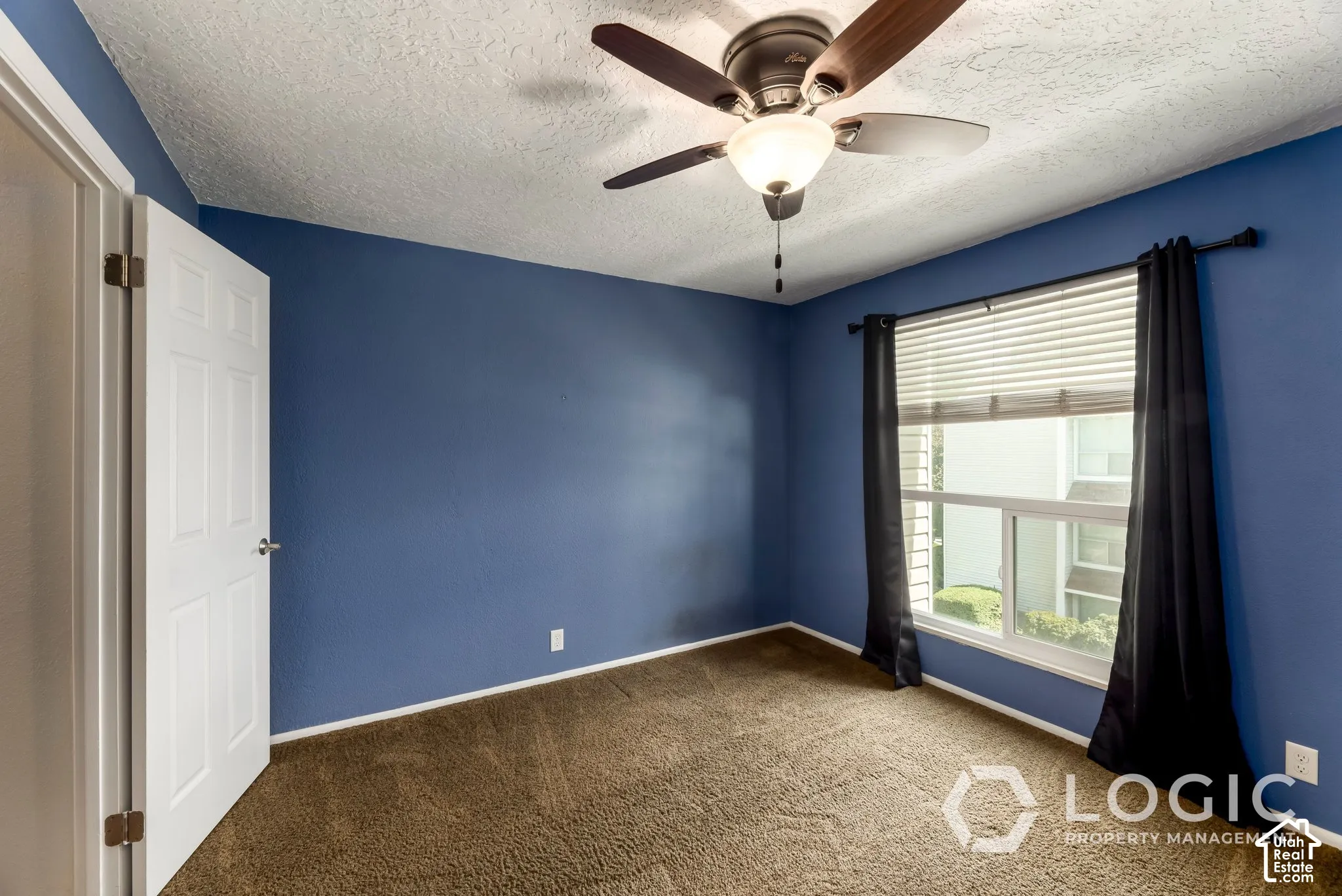 Window with blinds and drapes, ceiling fan with light fixture, textured ceiling, paneled interior door, and carpet flooring