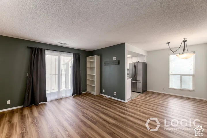 Wood-finish flooring throughout, sliding glass door with balcony access, built-in shelving, recessed kitchen area, and a traditional ceiling light fixture