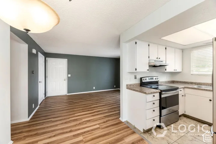 Kitchen featuring white cabinetry, stone-look countertops, stainless steel appliances, and wood-finish flooring