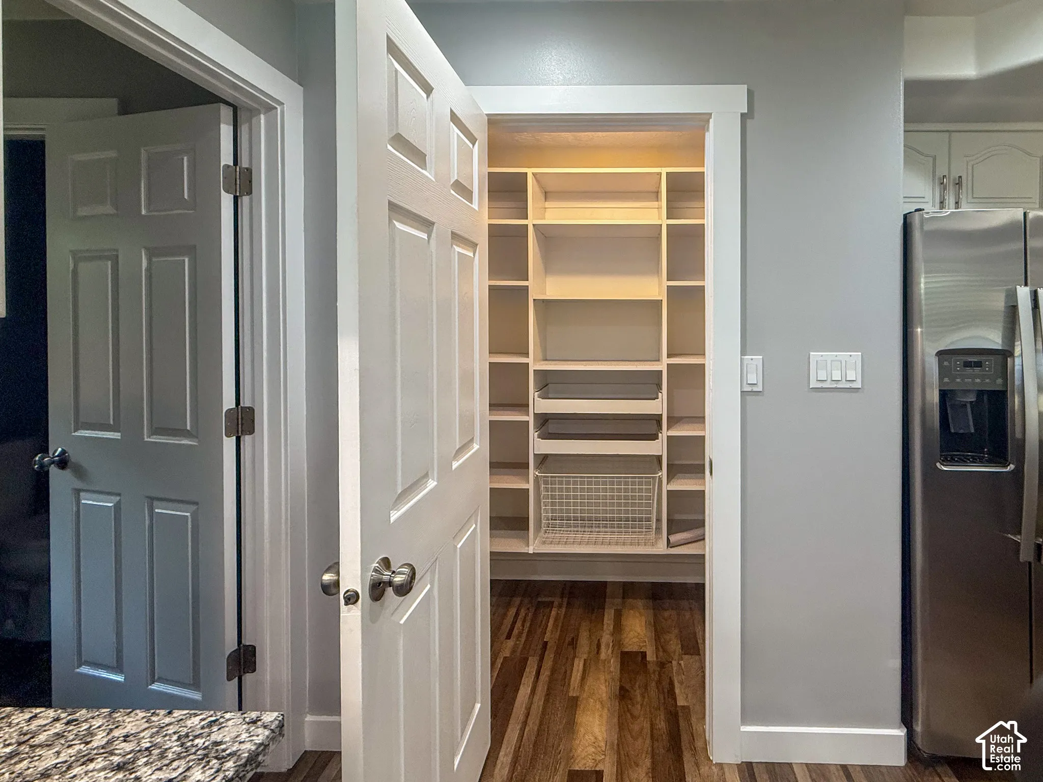 Walk-in pantry with extensive shelving, wood-finish flooring, and a stainless steel refrigerator