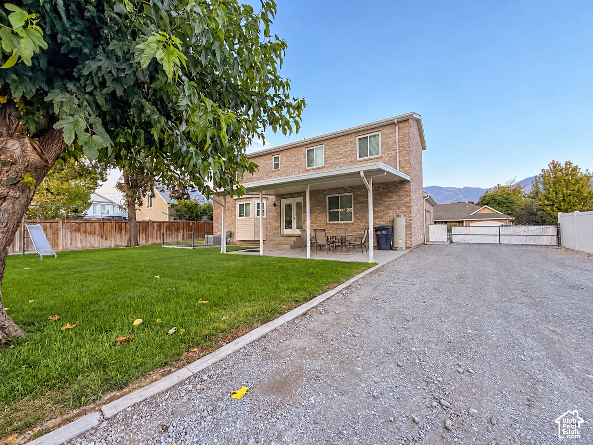 Brick exterior with white trim, covered patio, gravel driveway, and a fenced yard with a manicured lawn