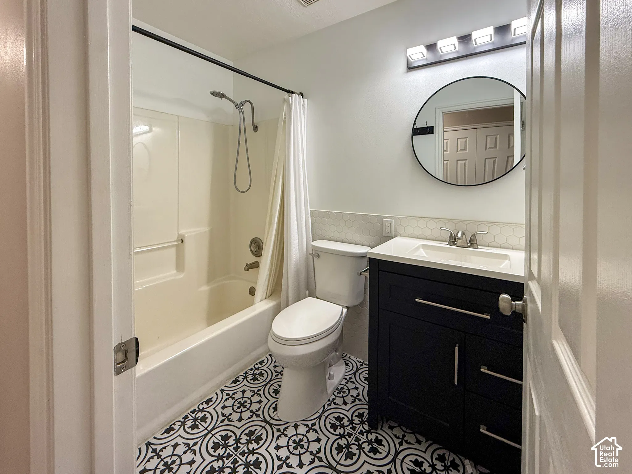 Bathroom featuring a tub/shower combination, decorative floor tiling, single vanity with under-sink storage, hexagon tile backsplash, and a wall-mounted light fixture