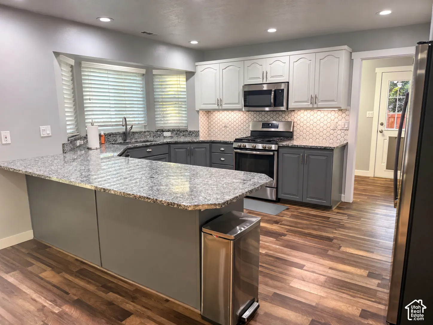 Kitchen featuring granite countertops, stainless steel appliances, two-tone cabinetry, wood-finish flooring, and a decorative tile backsplash