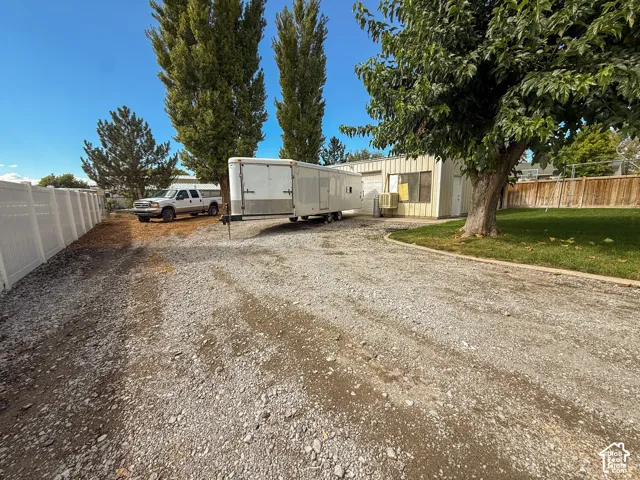 Gravel driveway providing substantial parking, white vinyl fencing, mature trees, and a wooden fence