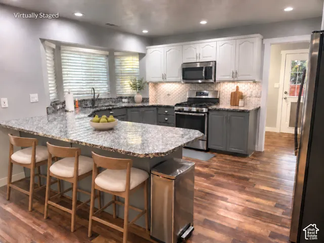 Kitchen featuring wood-finish flooring, a two-tone cabinetry scheme, stainless steel appliances, speckled countertops, and a tile backsplash
