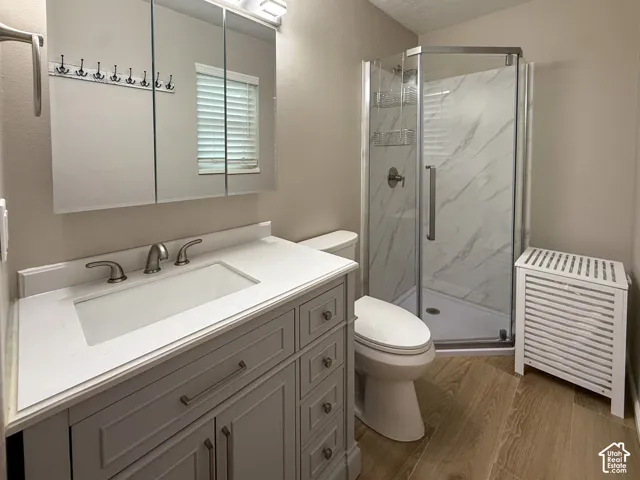 Primary Bath - Vanity with integrated sink and brushed nickel faucet, wall-mounted mirror cabinet, corner shower with glass enclosure and marble-look surround, and wood-finish flooring
