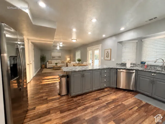 Wood-finish flooring throughout, kitchen island with gray cabinetry, stainless steel dishwasher, and light-toned countertops