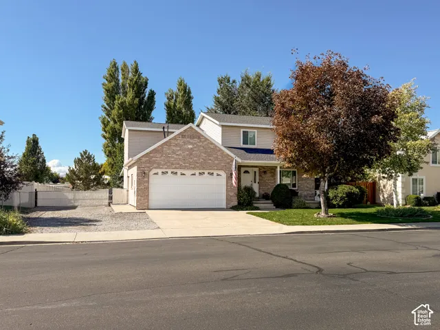Two-story residence featuring a two-car garage, stone and siding exterior, concrete driveway, and established front yard landscaping