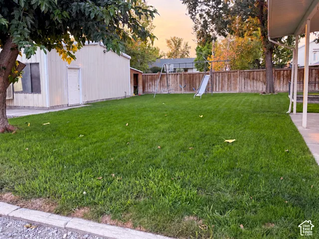 Expansive lawn area with a perimeter fence, mature trees, and a concrete patio