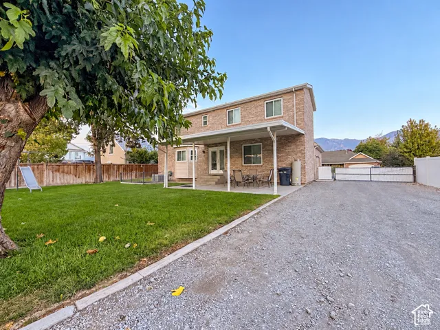 Brick exterior with white trim, covered patio, gravel driveway, and a fenced yard with a manicured lawn