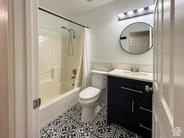 Bathroom featuring a tub/shower combination, decorative floor tiling, single vanity with under-sink storage, hexagon tile backsplash, and a wall-mounted light fixture