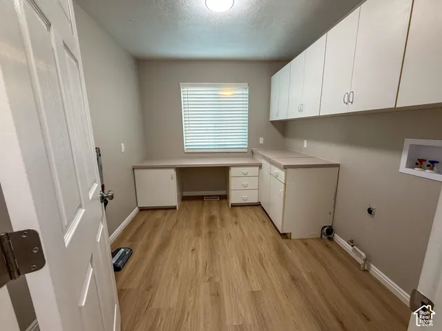 Wood-finish flooring, built-in white cabinetry, integrated desk space, upper wall-mounted white cabinets, and a window with blinds