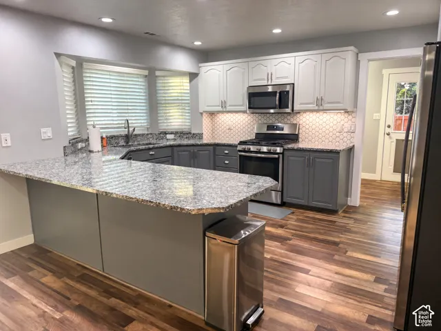 Kitchen featuring granite countertops, stainless steel appliances, two-tone cabinetry, wood-finish flooring, and a decorative tile backsplash