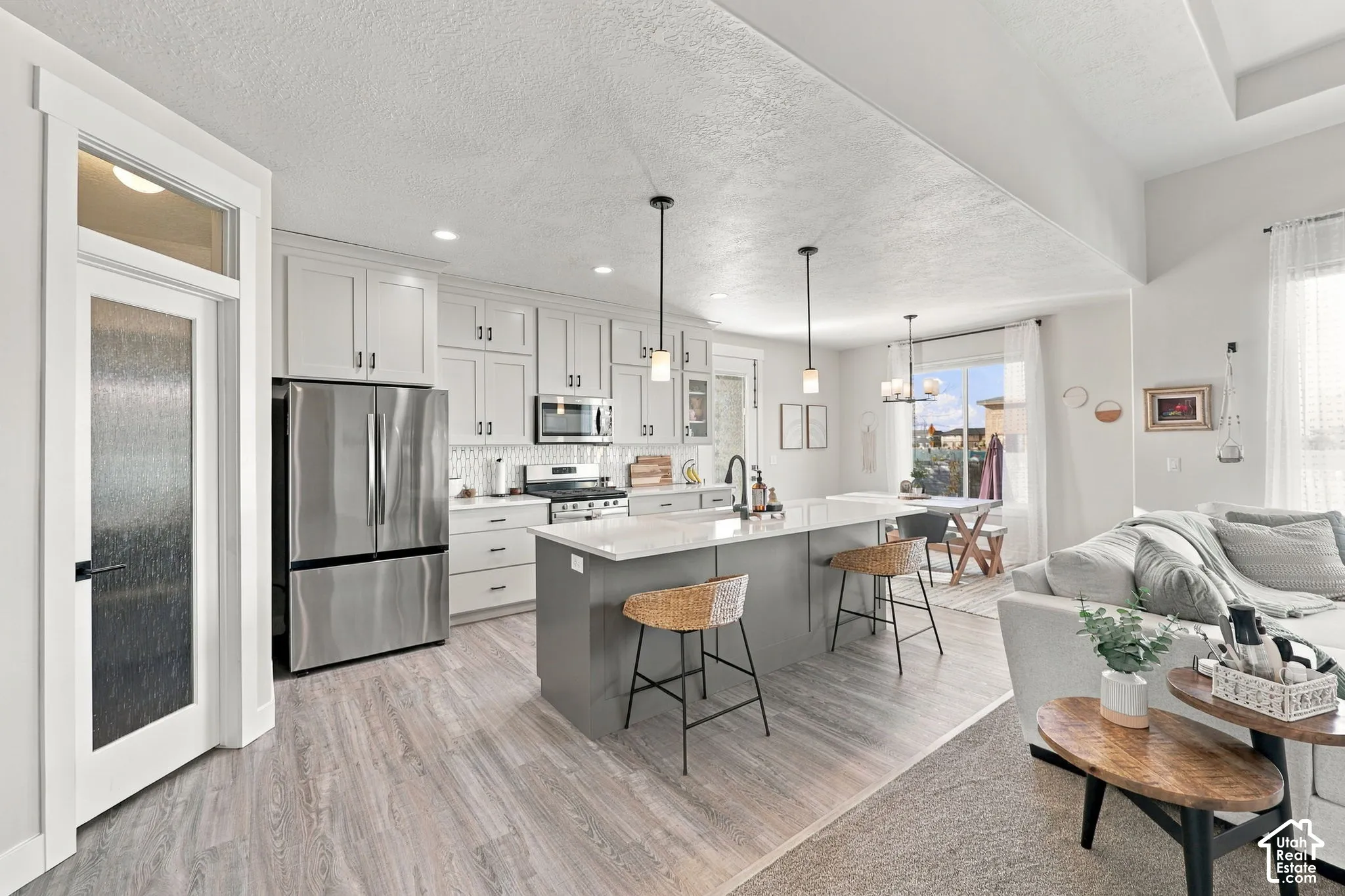 Open-concept kitchen featuring light-toned cabinetry, stainless steel appliances, a center island with pendant lighting, and wood-finish flooring