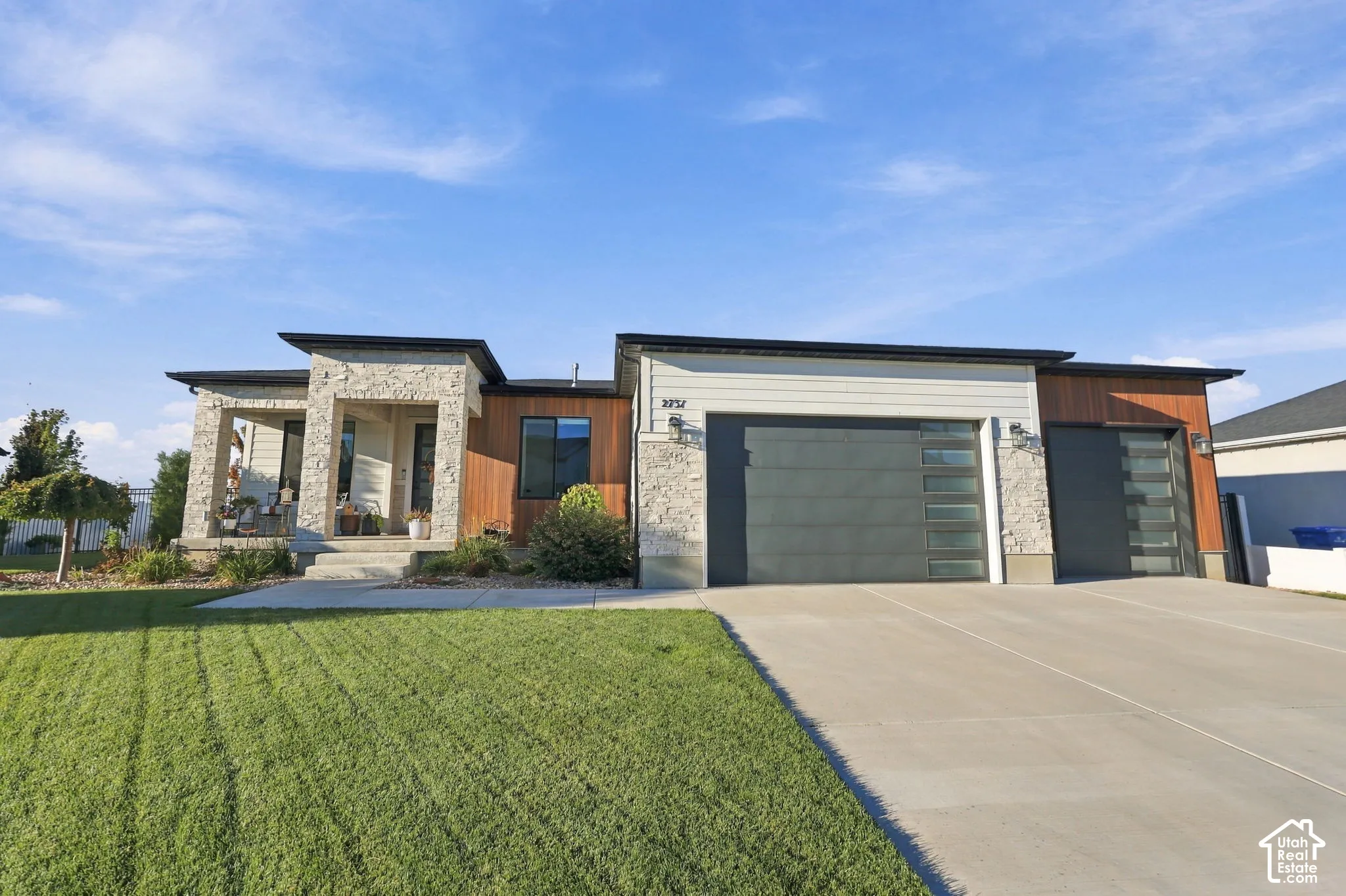 Modern exterior featuring stone and wood-look siding, a covered entry porch, and two garage doors with frosted glass panels