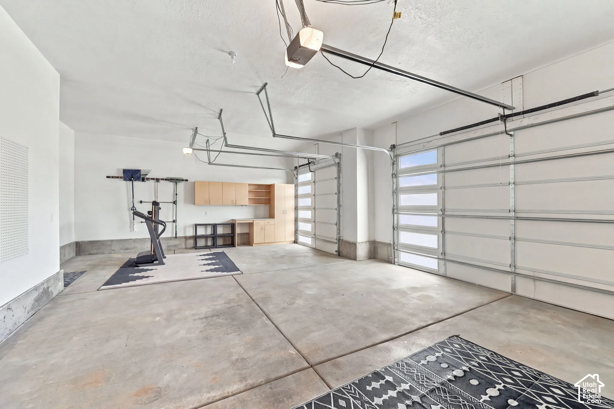 Expansive garage with concrete flooring, two overhead garage doors with frosted window panels, and built-in wood-finish cabinetry
