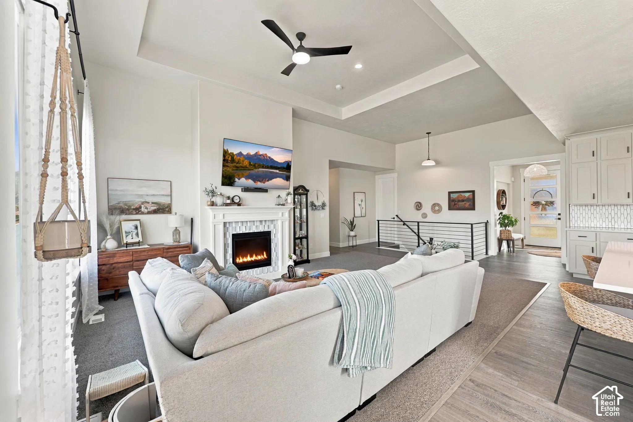 Recessed ceiling with an integrated fan, custom fireplace featuring a tile surround and mantel, and wood-finish flooring